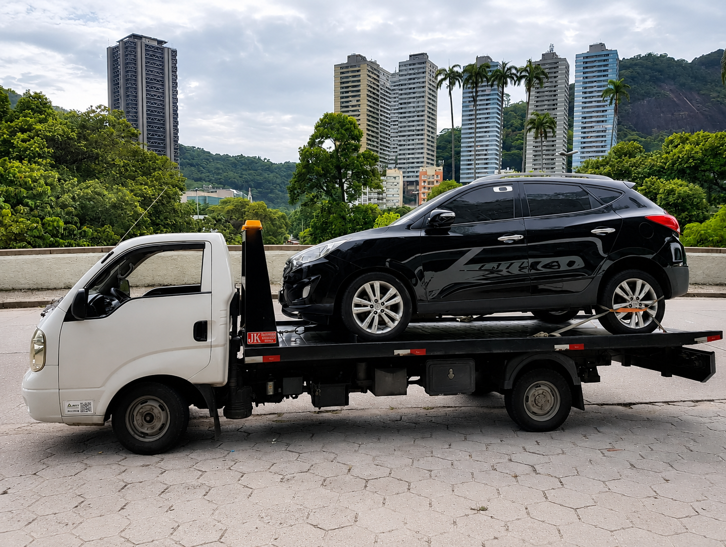 SUV preto sobre plataforma de reboque com prédios ao fundo