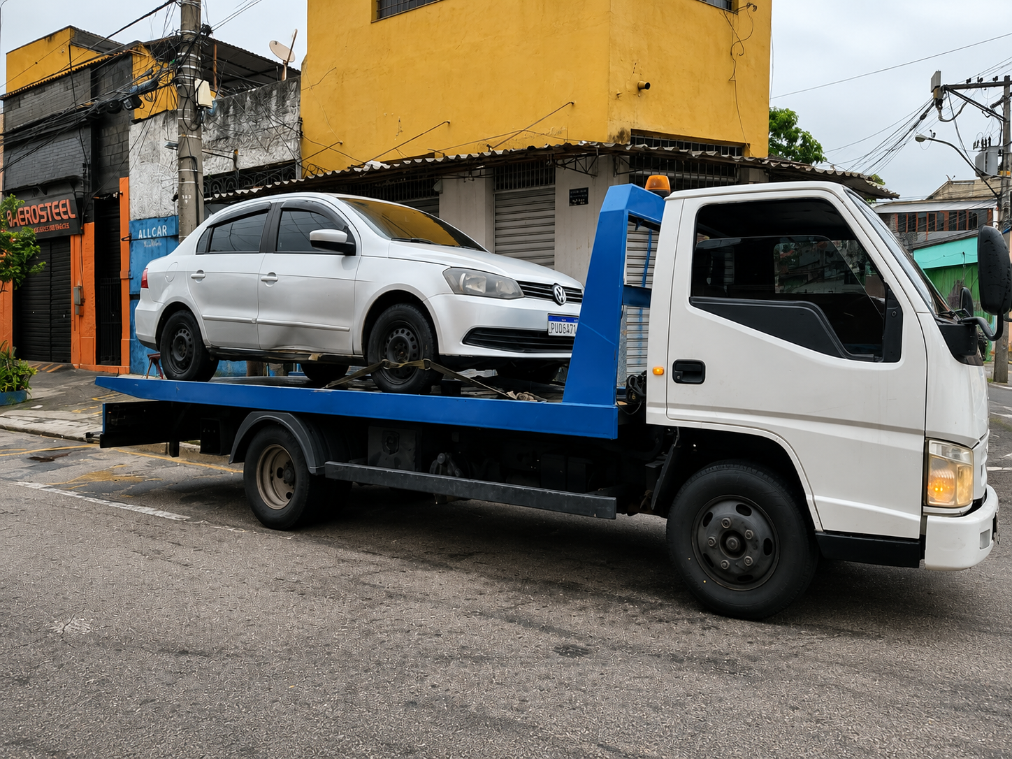 Sedã branco sobre plataforma azul de reboque em rua da cidade